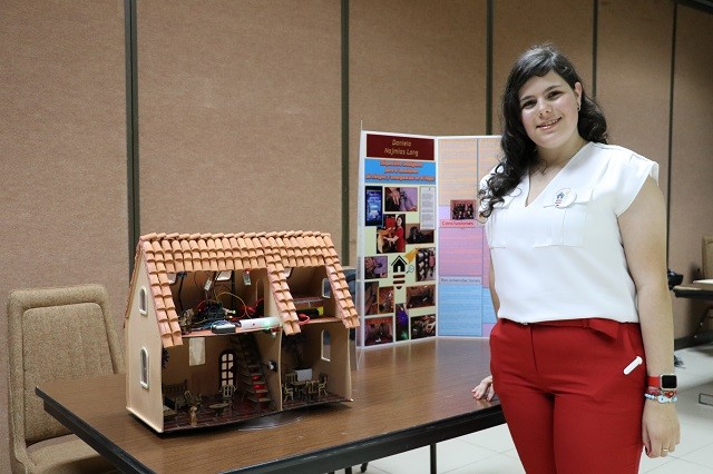 A model house wired with the DIMREH monitoring electronics beside the project poster at a Costa Rican science fair